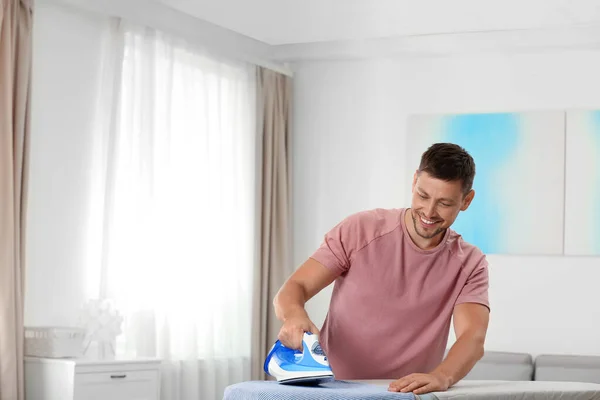 Bello uomo stiratura lavanderia pulita a casa, spazio per il testo — Foto Stock