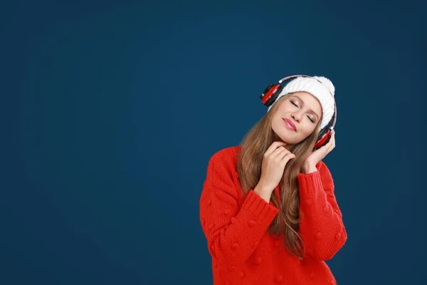 Young woman listening to music with headphones on dark blue background, space for text — Stock Photo, Image