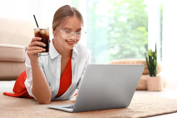 Mujer joven con un vaso de cola trabajando en el portátil en casa. Bebida refrescante —  Fotos de Stock