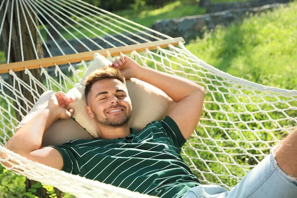 Hombre joven descansando en la hamaca cómoda en el jardín verde — Foto de Stock