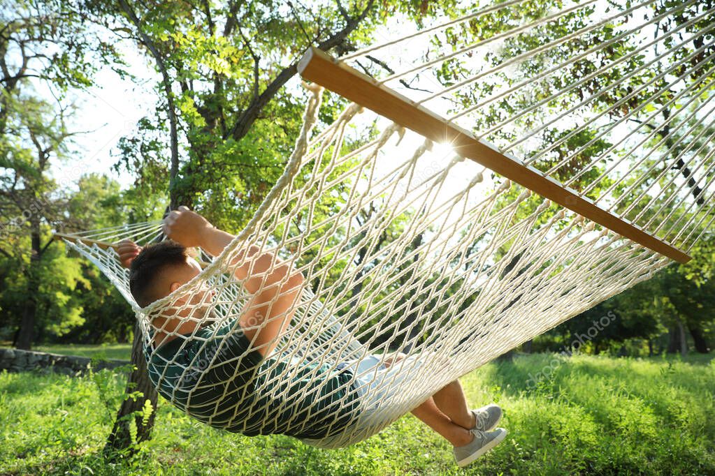 Young man resting in comfortable hammock at green garden