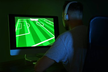 Karanlık odada modern bilgisayarda video oyunu oynayan kulaklıklı adam