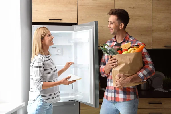 Pareja feliz poniendo productos en el refrigerador en casa — Foto de Stock