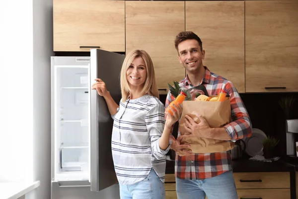 Mutfakta buzdolabının yanında bir çanta dolusu ürünleri olan mutlu bir çift. — Stok fotoğraf