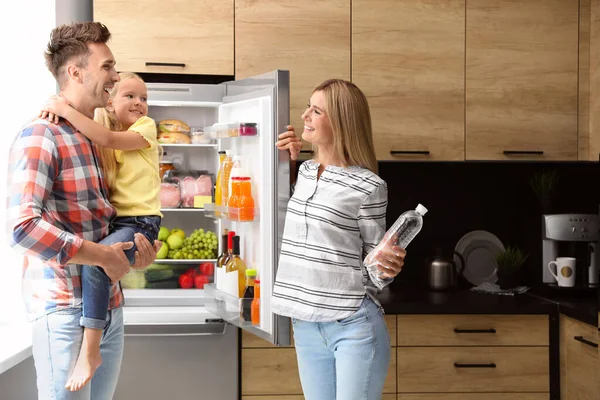 Família feliz com garrafa de água perto da geladeira na cozinha — Fotografia de Stock