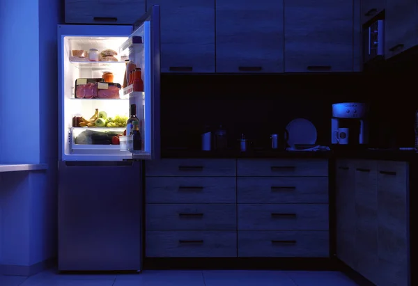 Open refrigerator full of products in kitchen at night — Stock Photo, Image