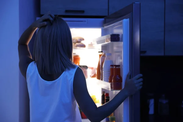 Žena dívá do ledničky plné výrobků v noci — Stock fotografie