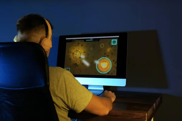 Hombre con auriculares jugando videojuego en la computadora moderna en la habitación oscura —  Fotos de Stock