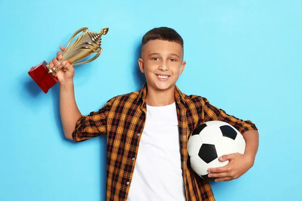 Gelukkige jongen met gouden winnende beker en voetbal bal op blauwe achtergrond — Stockfoto