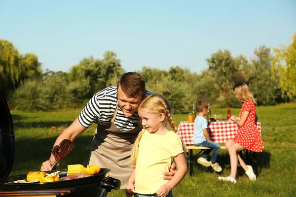 Padre con bambina al barbecue e la loro famiglia nel parco — Foto Stock