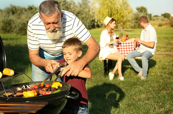 Bunicul cu un băiețel gătit mâncare pe grătar și familia lor în parc — Fotografie, imagine de stoc