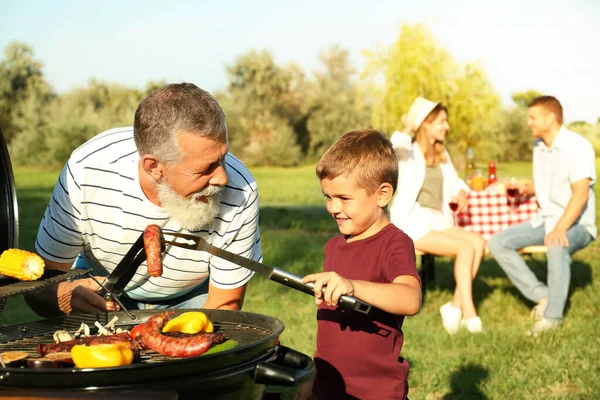 Bunicul cu un băiețel gătit mâncare pe grătar și familia lor în parc — Fotografie, imagine de stoc