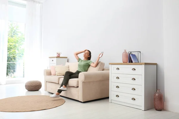 Feliz joven mujer encendiendo el aire acondicionado con control remoto en casa — Foto de Stock