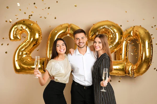 Jovens amigos felizes perto de ouro 2020 balões em fundo bege. Celebração de Ano Novo — Fotografia de Stock