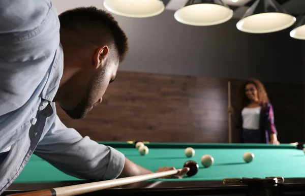 Young man playing billiard and blurred African-American woman on background. Space for text — Stock Photo, Image