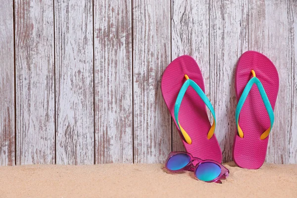 Bright flip flops and sunglasses on sand near wooden wall, space for text. Summer beach accessories — Stock Photo, Image