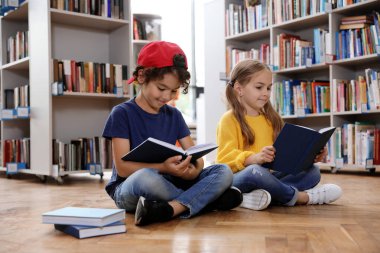 Kütüphanede yerde kitap okuyan şirin küçük çocuklar.