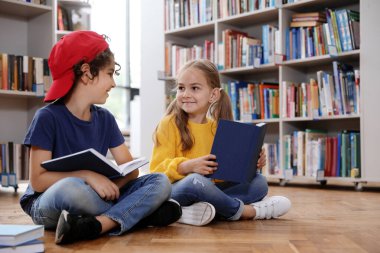 Kütüphanede yerde kitap okuyan şirin küçük çocuklar.