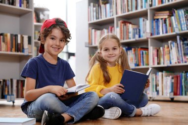 Kütüphanede yerde kitap okuyan şirin küçük çocuklar.