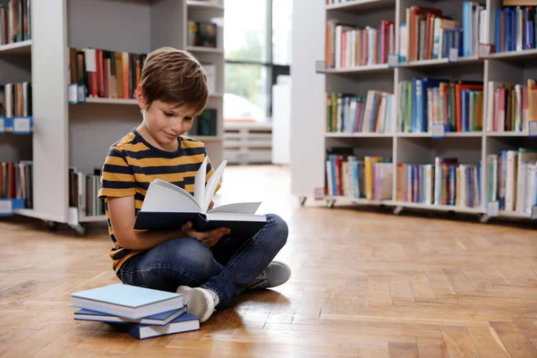 Bonito menino leitura livro no chão na biblioteca — Fotografia de Stock