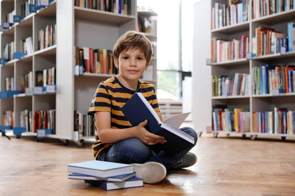 Bonito menino leitura livro no chão na biblioteca — Fotografia de Stock