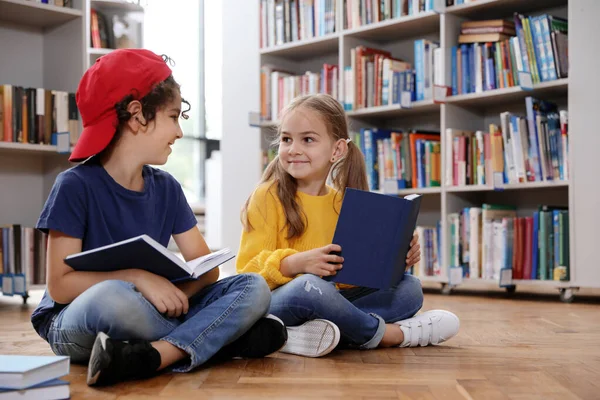 Lindos niños pequeños leyendo libros en el suelo en la biblioteca —  Fotos de Stock