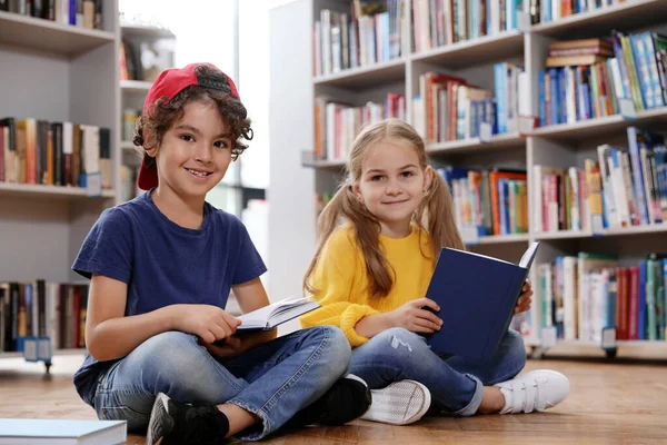 Roztomilé malé děti čtení knih na podlaze v knihovně — Stock fotografie