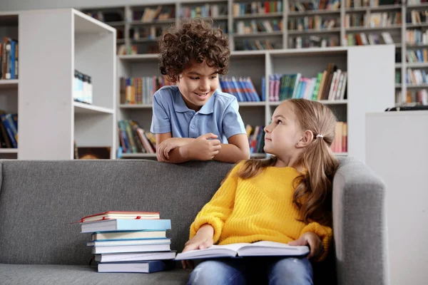Niños pequeños y felices leyendo el libro en el sofá en la biblioteca — Foto de Stock