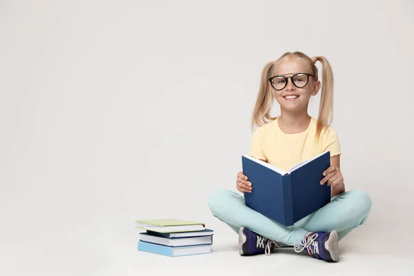 Linda niña con gafas libro de lectura sobre fondo gris. Espacio para texto — Foto de Stock