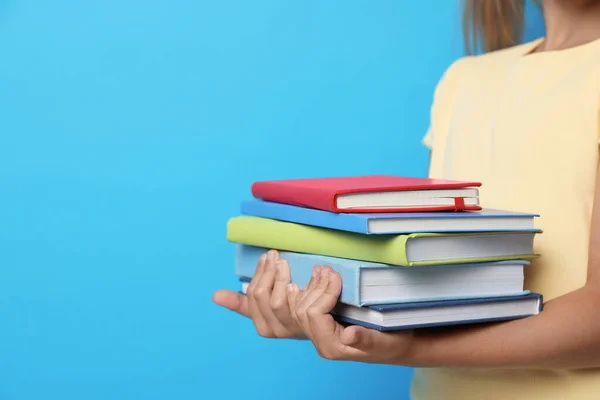 Ragazzina che tiene libri su sfondo blu, primo piano. Concetto di lettura — Foto Stock