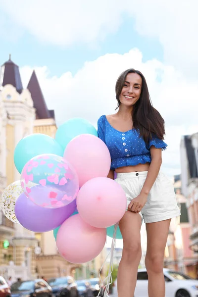 Piękna młoda kobieta z kolorowymi balonami na ulicy miasta — Zdjęcie stockowe