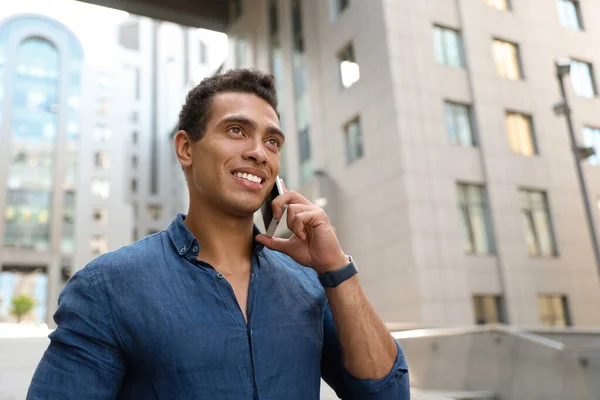 Portrait of handsome young African-American man talking on mobile phone outdoors. Space for text