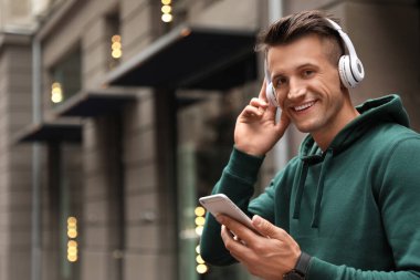 Şehir caddesinde müzik dinleyen kulaklıklı ve akıllı telefonlu yakışıklı bir adamın portresi. Metin için boşluk
