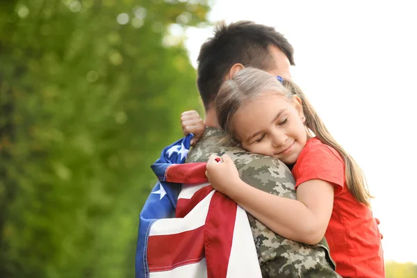 Vater in Militäruniform mit amerikanischer Flagge umarmt seine kleine Tochter im grünen Park — Stockfoto