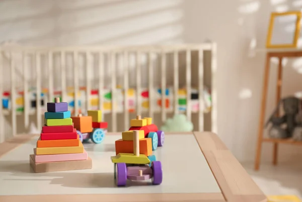 Juguetes de madera brillantes en la mesa en el acogedor interior de la habitación del bebé — Foto de Stock