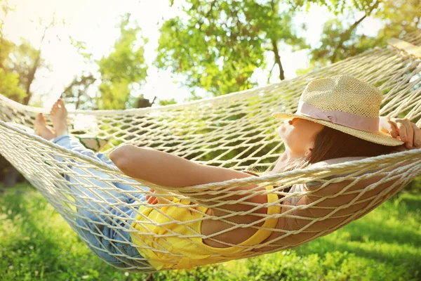 Młoda kobieta z kapeluszem odpoczynku w wygodnym hamaku w zielonym ogrodzie — Zdjęcie stockowe