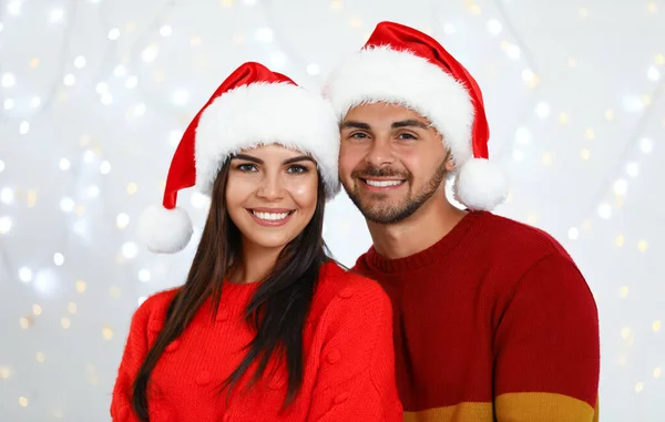 Casal jovem encantador em chapéus de Papai Noel contra luzes festivas borradas. Celebração de Natal — Fotografia de Stock