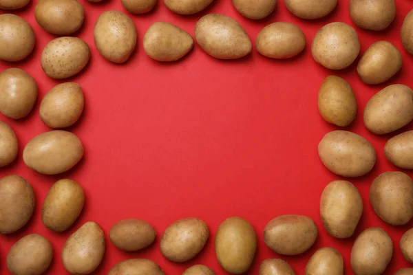 Frame gemaakt van rauwe verse biologische aardappelen op rode ondergrond, plat gelegd. Ruimte voor tekst — Stockfoto
