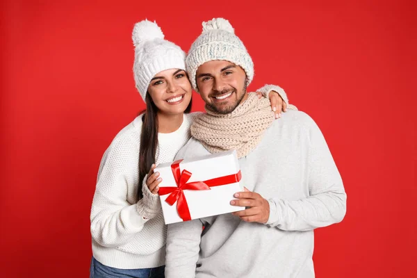 Bella giovane coppia con scatola regalo su sfondo rosso. Celebrazione di Natale — Foto Stock