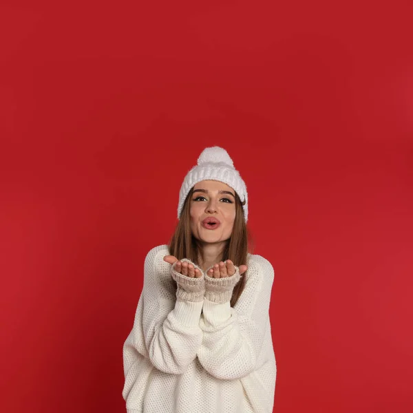 Krásná mladá žena v bílém svetru a klobouk na červeném pozadí. Zimní sezóna — Stock fotografie