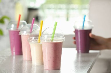 Beyaz ahşap masada plastik bardaklarda farklı milkshake 'ler.