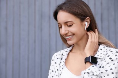 Gri duvarın yanında müzik dinleyen kablosuz kulaklıklı genç bir kadın. Metin için boşluk