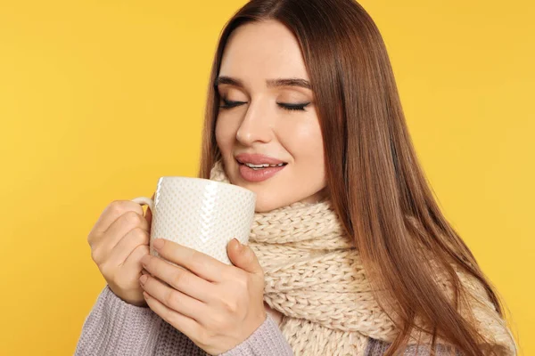 Krásná mladá žena ve svetru s pitím na žlutém pozadí. Zimní sezóna — Stock fotografie
