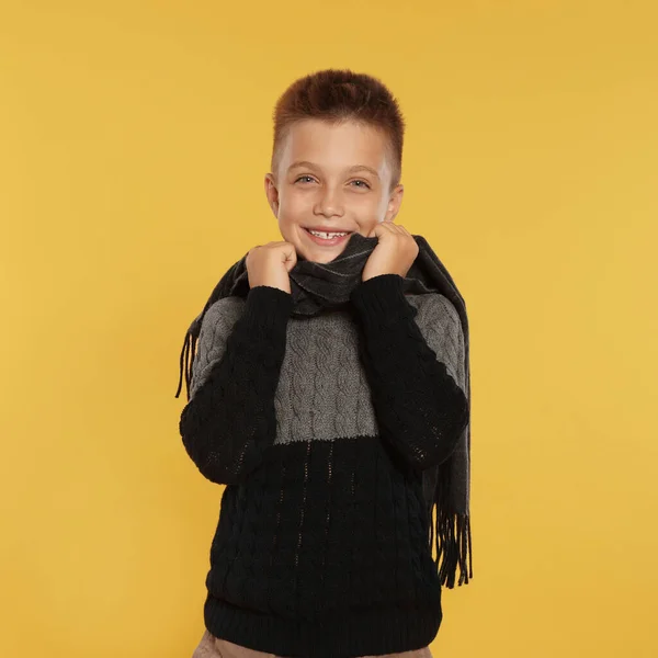 Leuk jongetje in warme trui en sjaal op gele achtergrond. Winterseizoen — Stockfoto