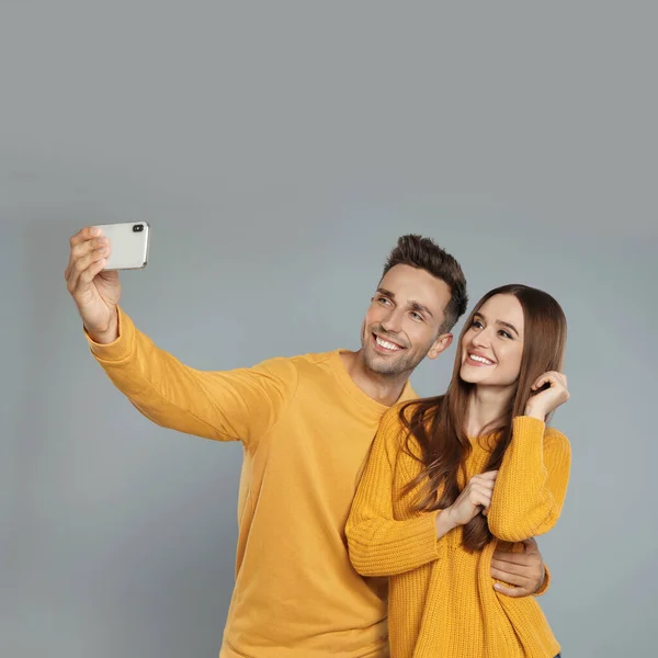 Joyeux jeune couple en vêtements chauds prenant selfie sur fond gris. Saison d'hiver — Photo