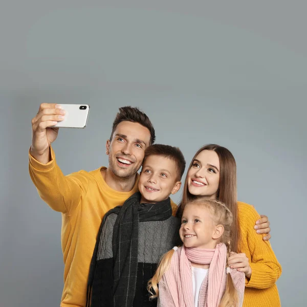 Família feliz em roupas quentes tomando selfie em fundo cinza. Temporada de Inverno — Fotografia de Stock