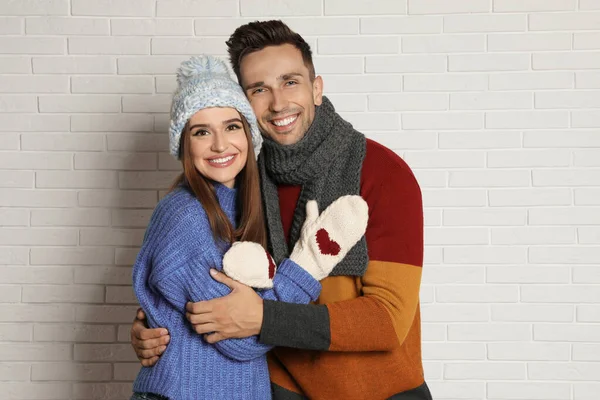 Feliz pareja joven en ropa de abrigo cerca de la pared de ladrillo blanco. Temporada de invierno — Foto de Stock