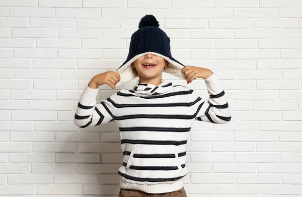 Słodki chłopczyk w kapeluszu i swetrze przy białej ceglanej ścianie. Sezon zimowy — Zdjęcie stockowe
