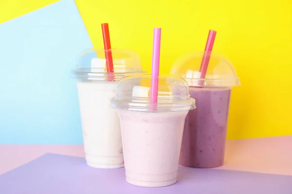 Verschiedene leckere Milchshakes in Plastikbechern auf farbigem Hintergrund — Stockfoto