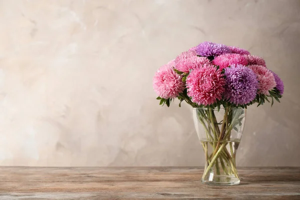 Glass vase with beautiful aster flowers on wooden table against beige background. Space for text — Stock Fotó